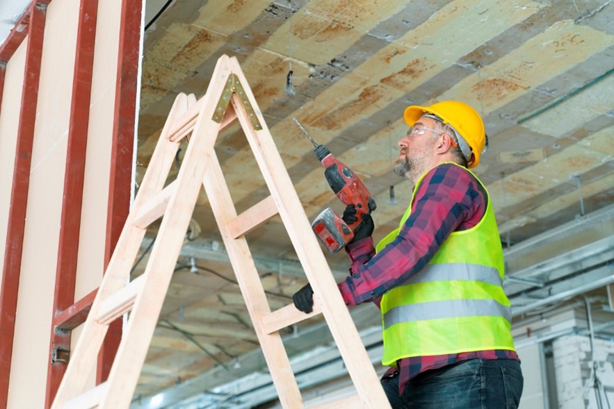 A man working at height using a drill up a ladder